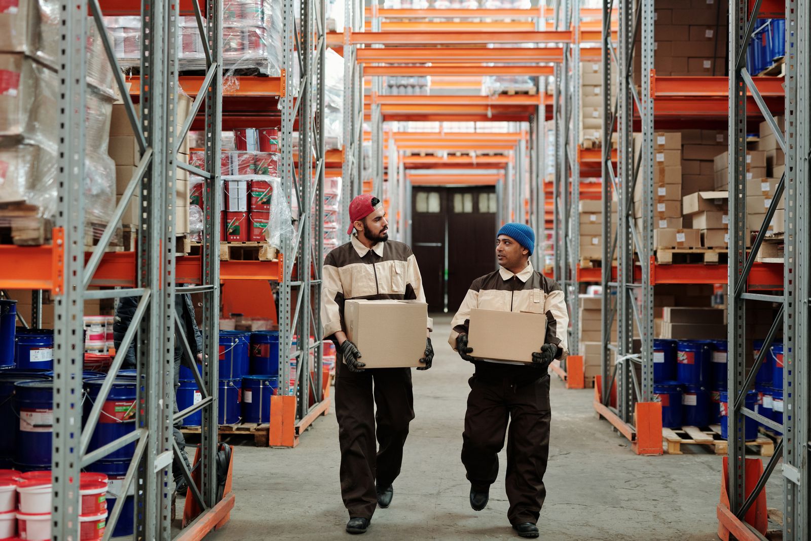 Warehouse workers in safety vests carrying boxes through a storage facility